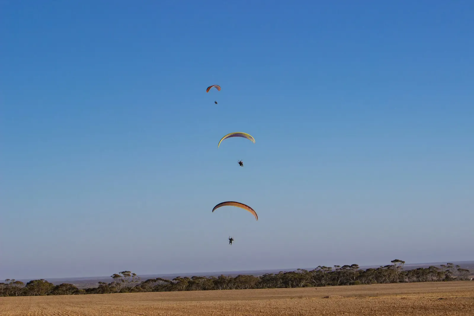 Three powered paragliders flying low over a dry field