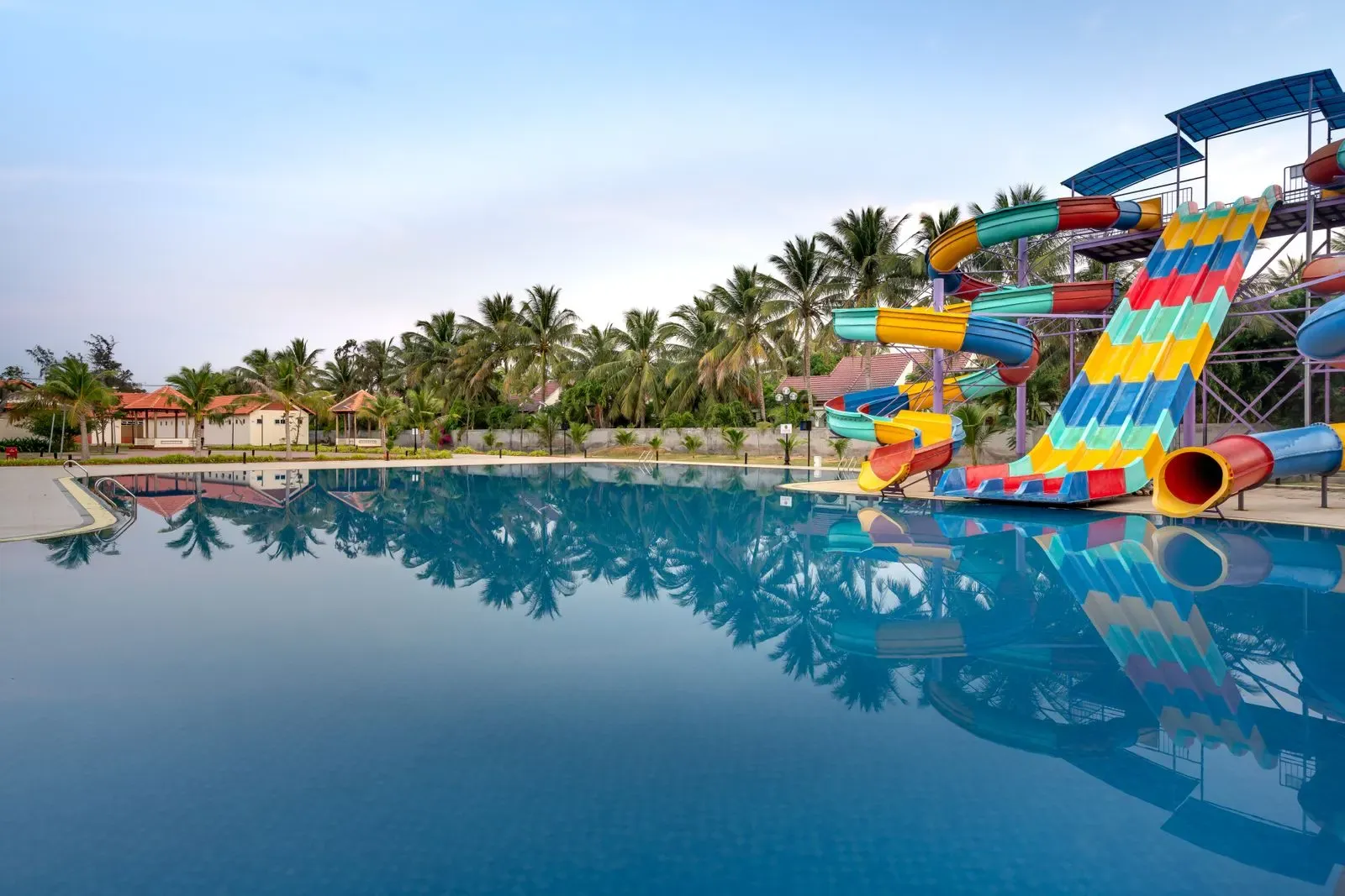A large pool reflecting palm trees, with colourful slide towers