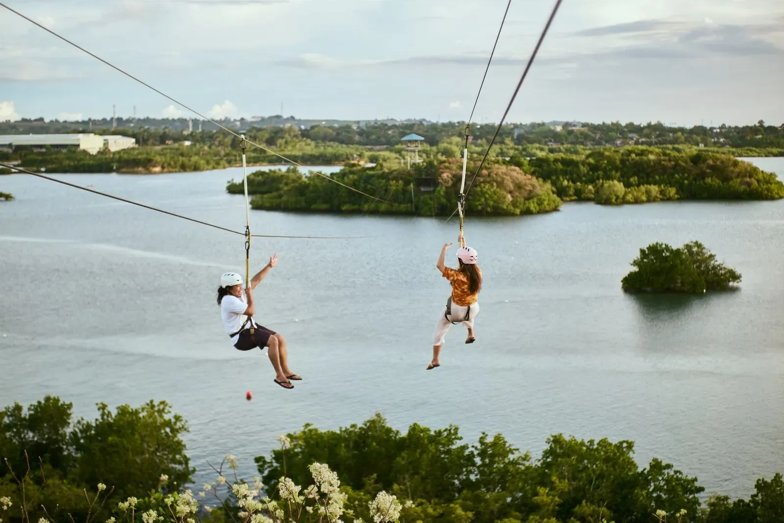 Two people ziplining over a lagoon