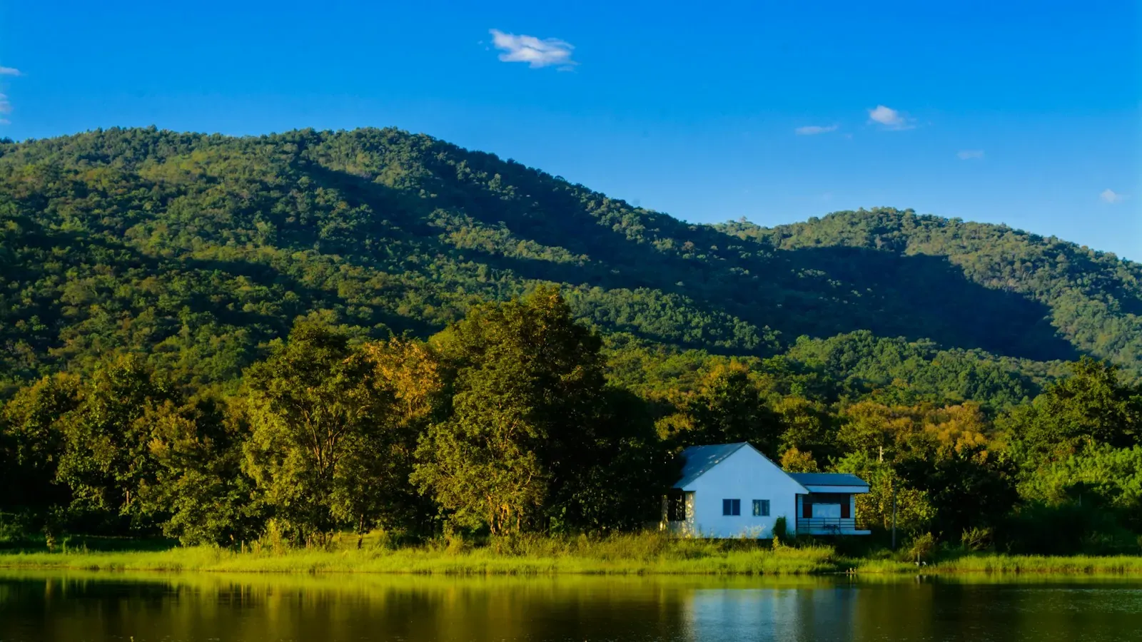 A lake with a small white house and green mountains under a blue sky