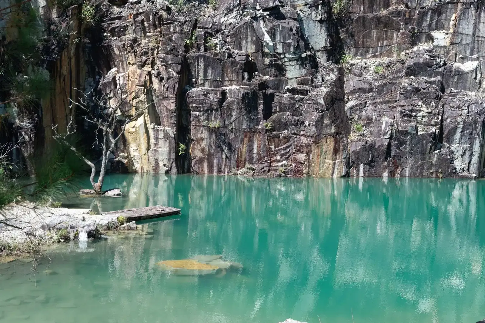 A turquoise quarry lake under a dark rock cliff