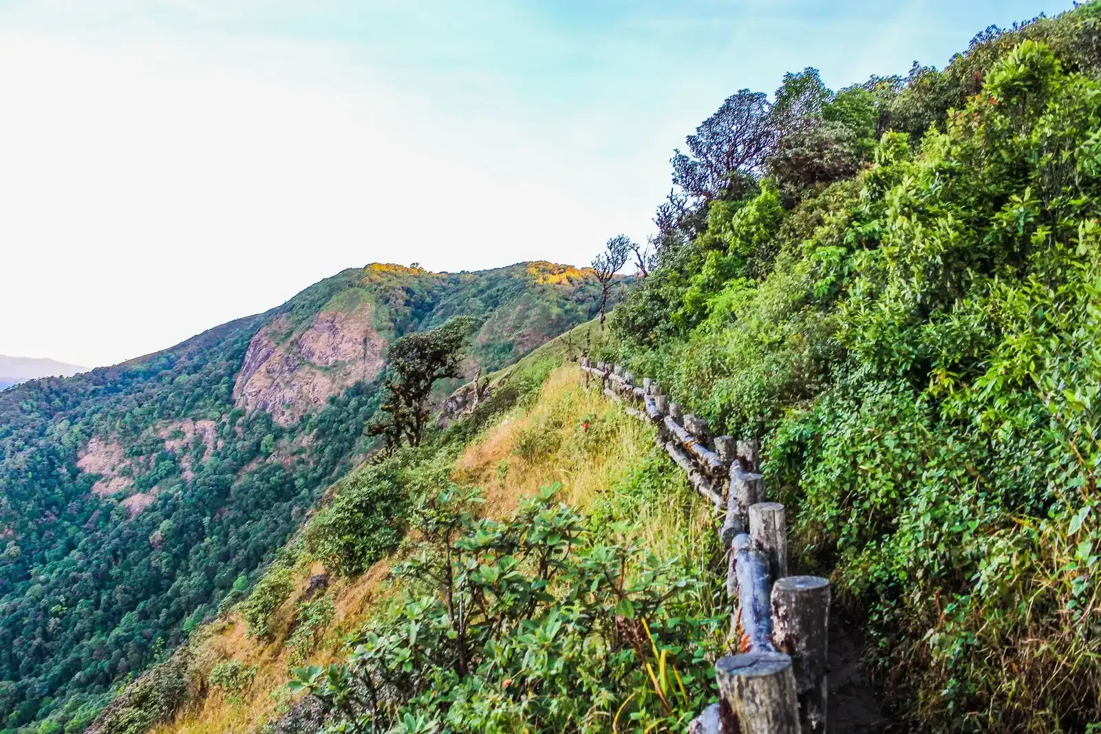 A ridge trail with a wooden handrail along grassy slopes
