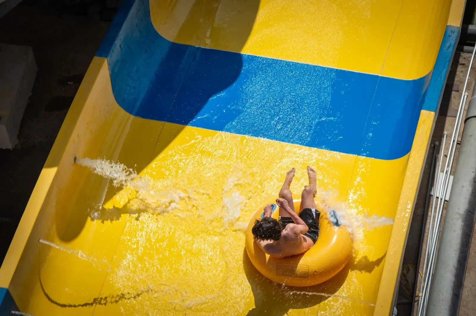 A man on a tube sliding down a yellow and blue water slide, seen from above