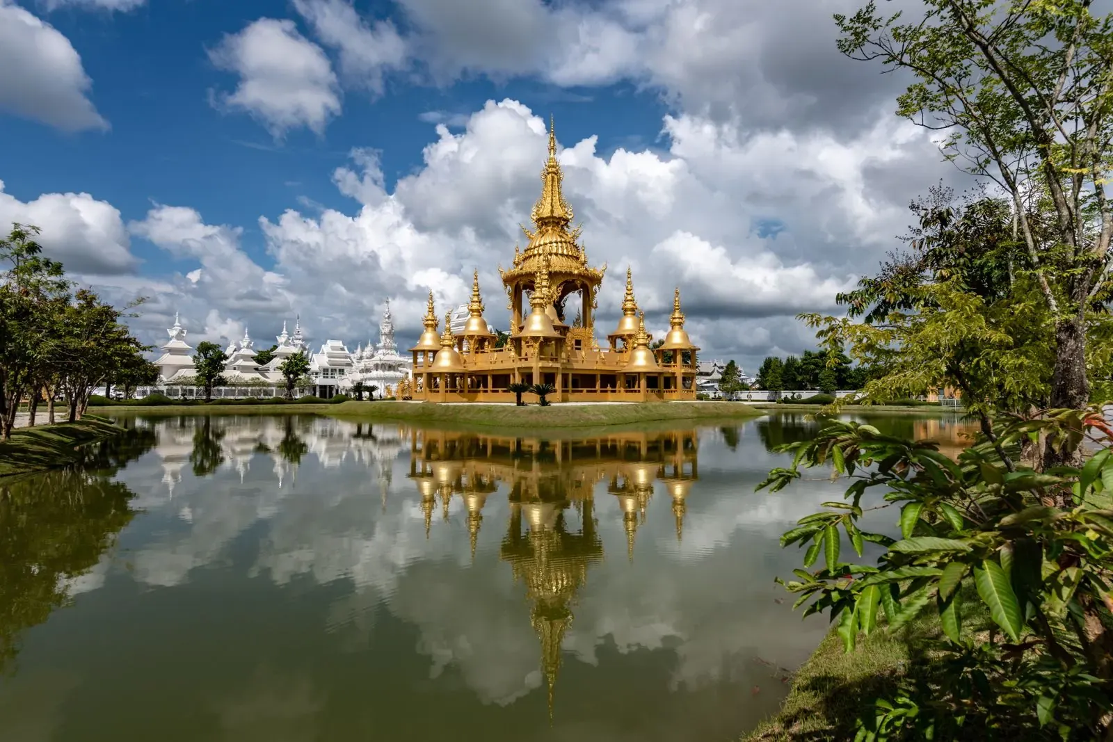 An ornate gold building reflected in a pond on the temple grounds
