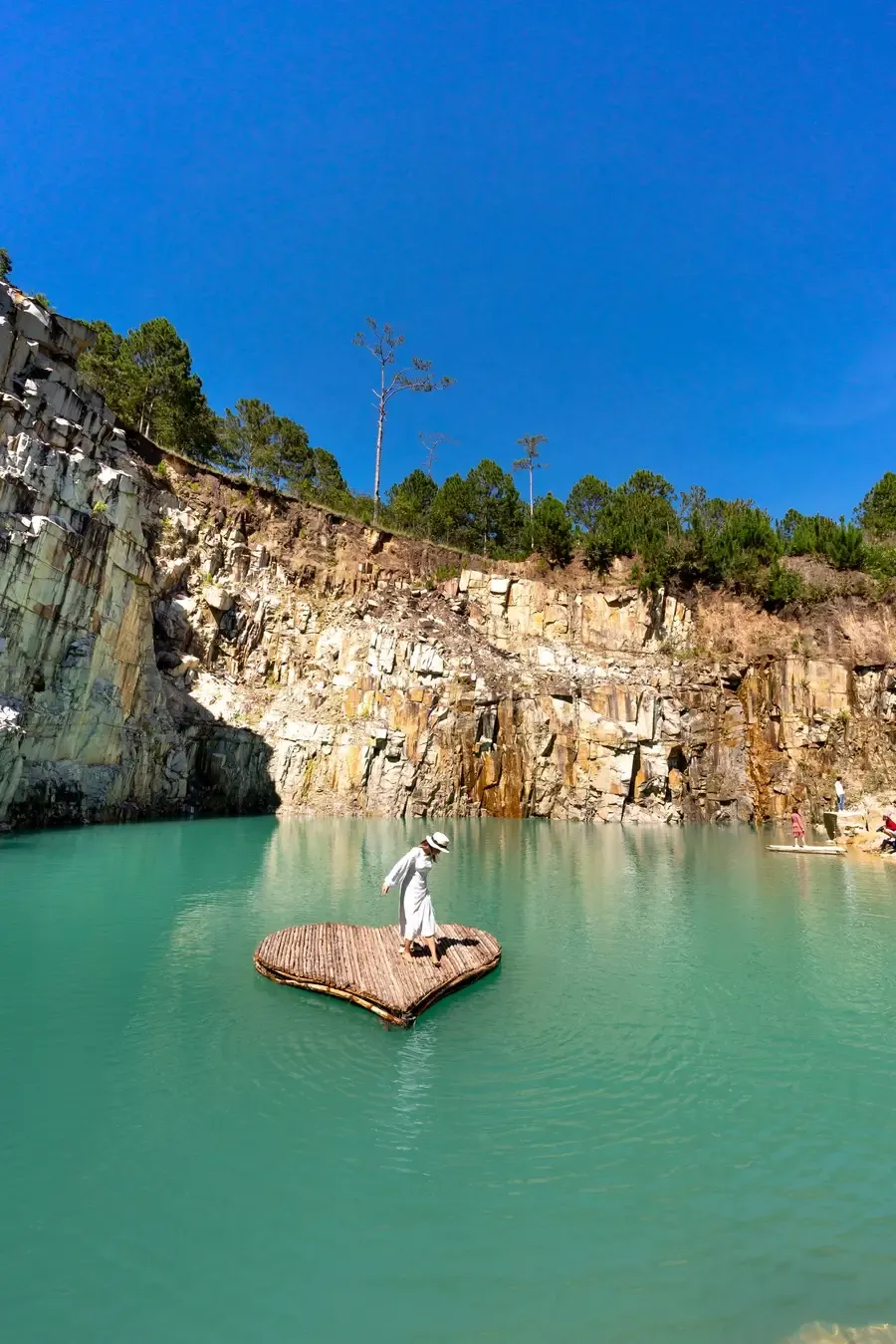 A person on a heart-shaped raft in a turquoise quarry lake under cliffs