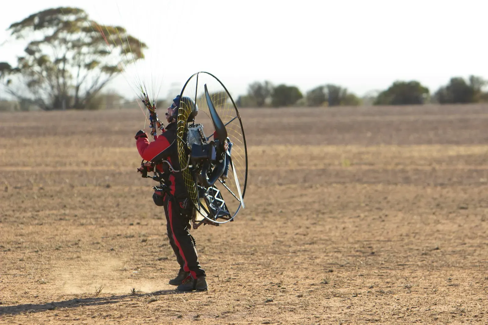 A pilot standing on a field with a paramotor on his back